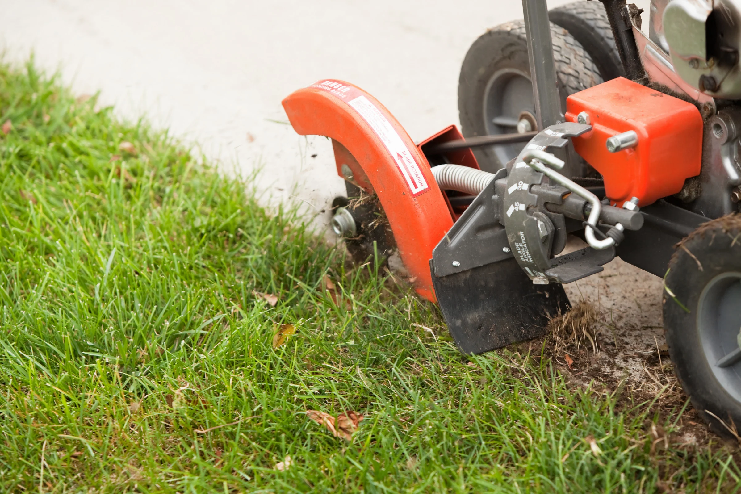 Power lawn edger creating a clean edge along a concrete walkway